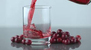 Pouring Cranberry Juice into a plain Glass tumbler with loose cranberries lying on the table