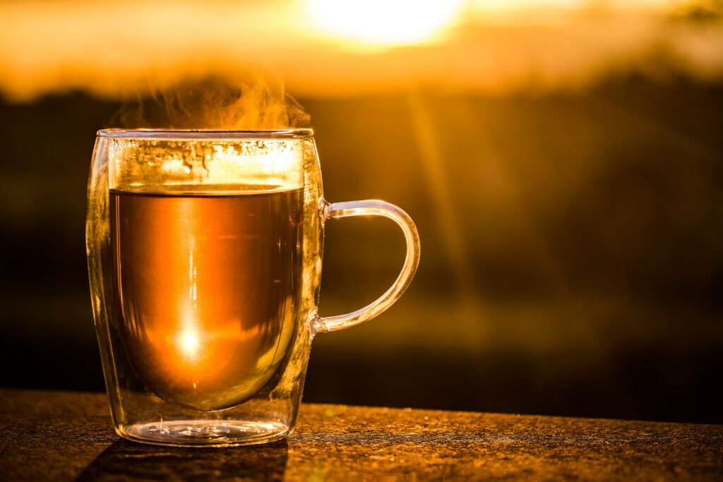 A Nice Glass mug full of Green tea perched on the edge of a table with the sun setting in the back ground.
