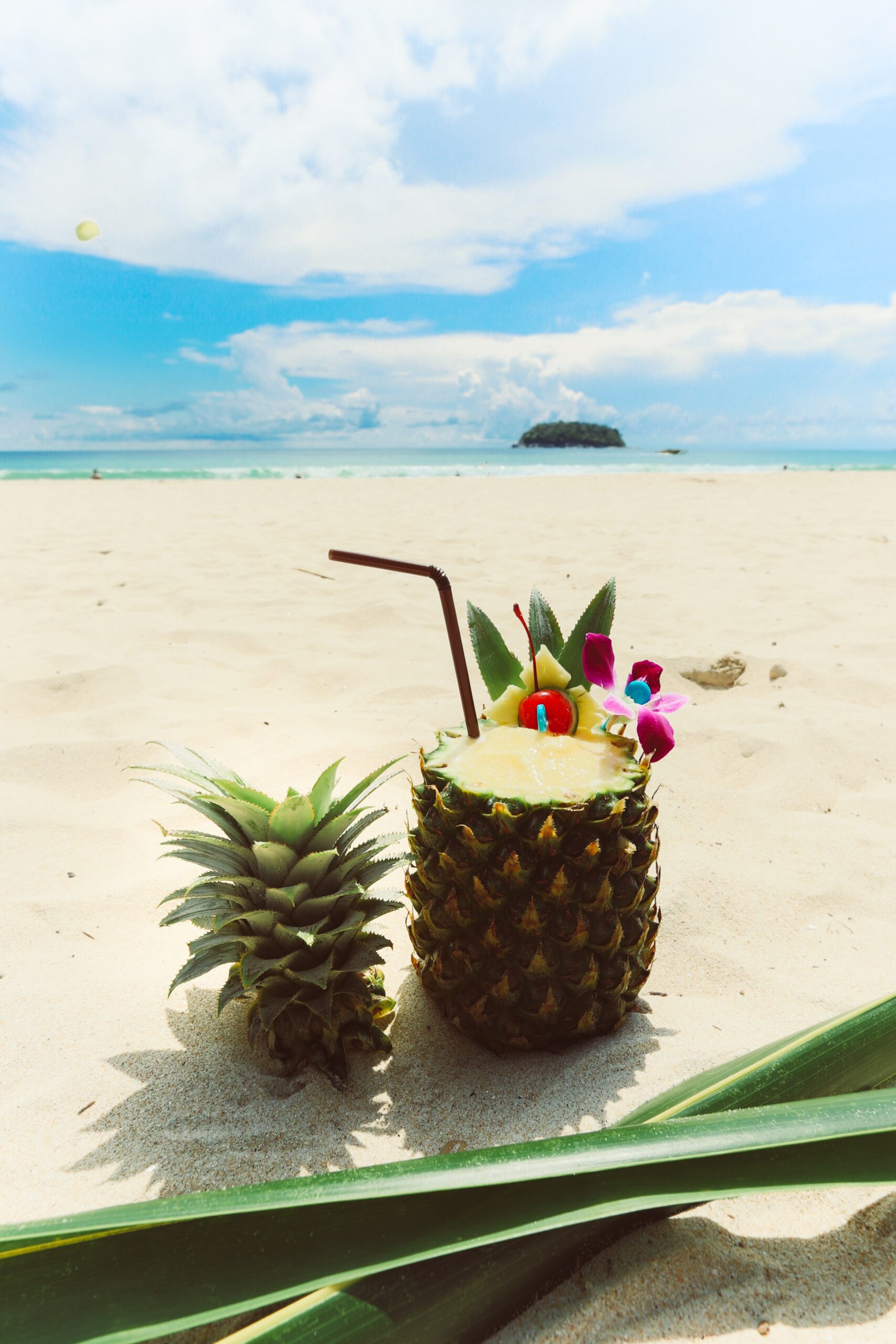 Pineapple with Top Cut Off and Straw for drinking out the juice on the beach with a beautiful blue sky in the background