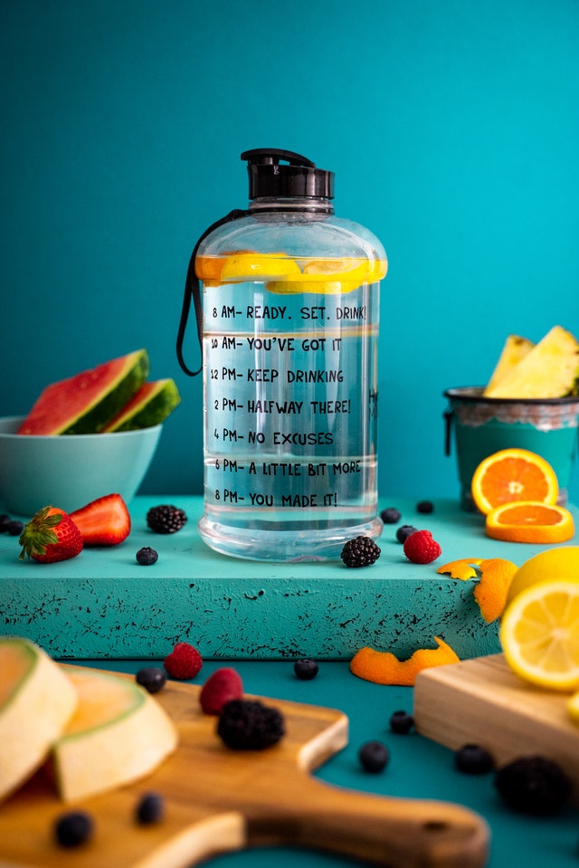 A bottle of Water with lemons inside and Various Fruits such as oranges ,apples ,Respberries.blackberries and water melon cut and lying on Boards.