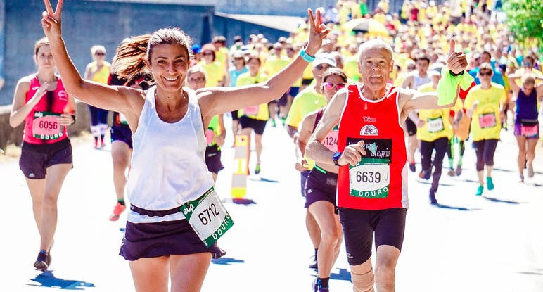 Lady and Man smiling and waving to crowd whilst running in a Race.